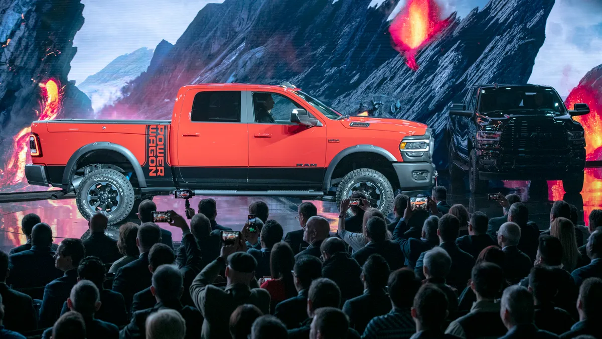 A hurge red pickup truck center staged, another huge pickup truck stage right, and people in the audience.