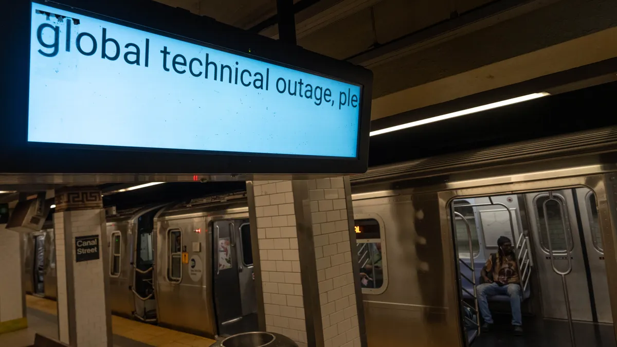 a screen hangs above a subway station, showing the words "global technical outage"