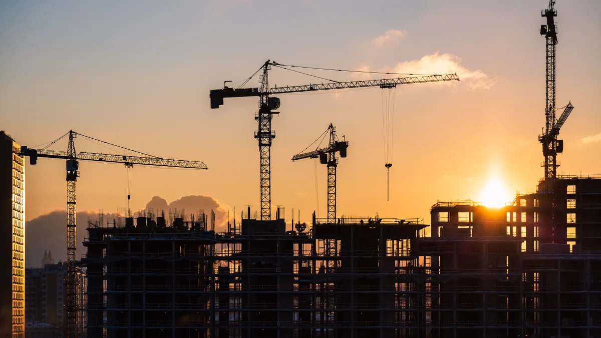 Building and construction cranes silhouetted against a yellow orange sky.