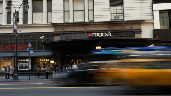 Blurry cars drive by a Macy's store entrance.