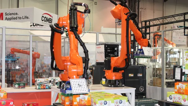 Two orange robot arms handle food packages on a conference floor.