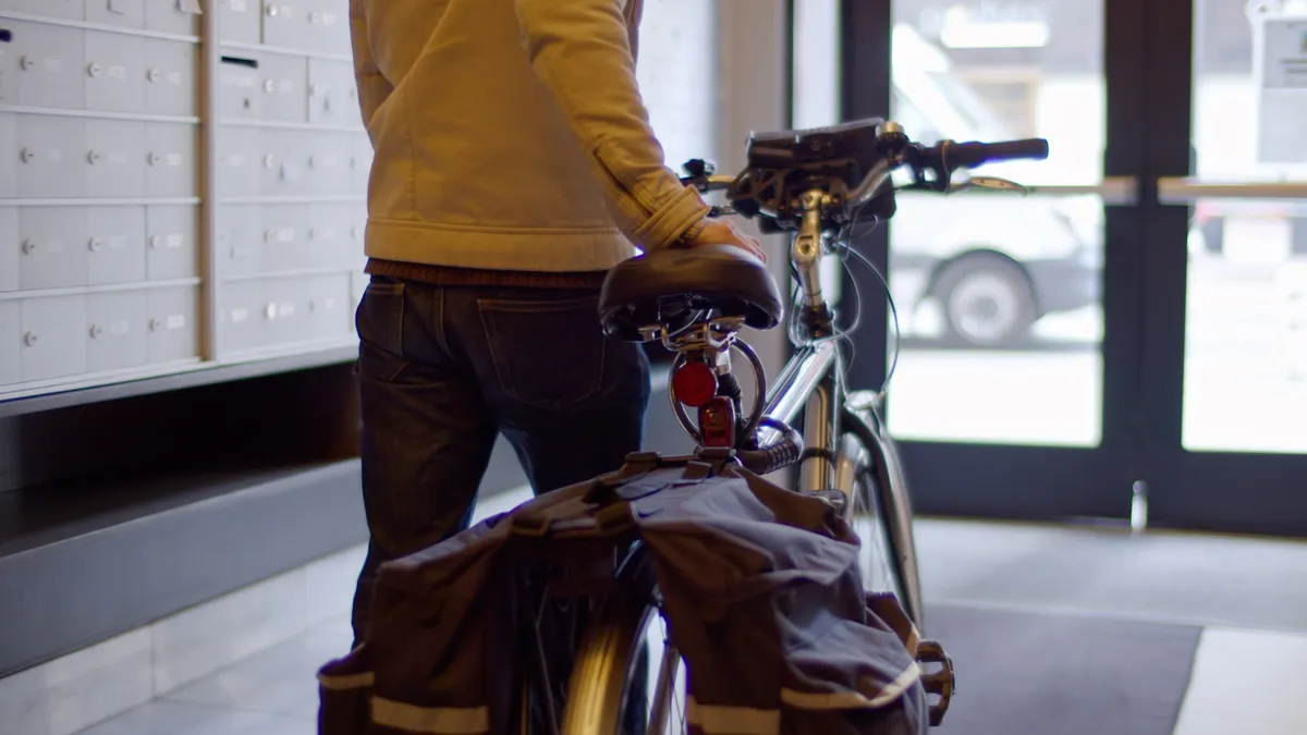 A person walking an electric bike out of an apartment building lobby.