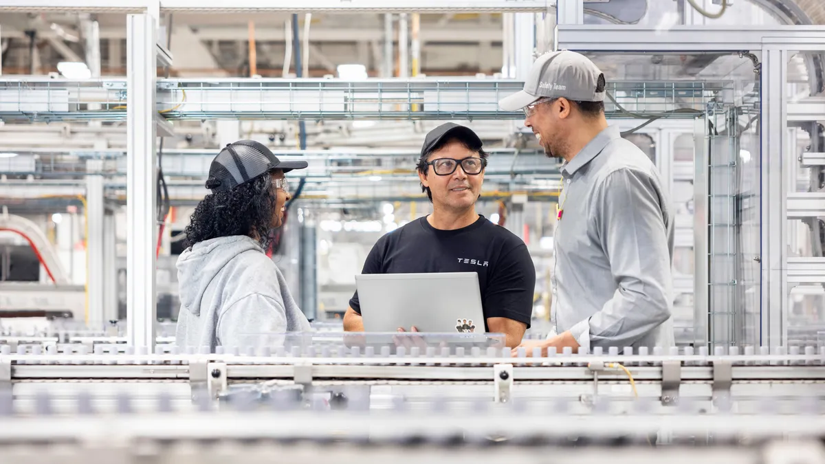 Three Tesla workers conversing at the company's EV factory in Fremont, California.