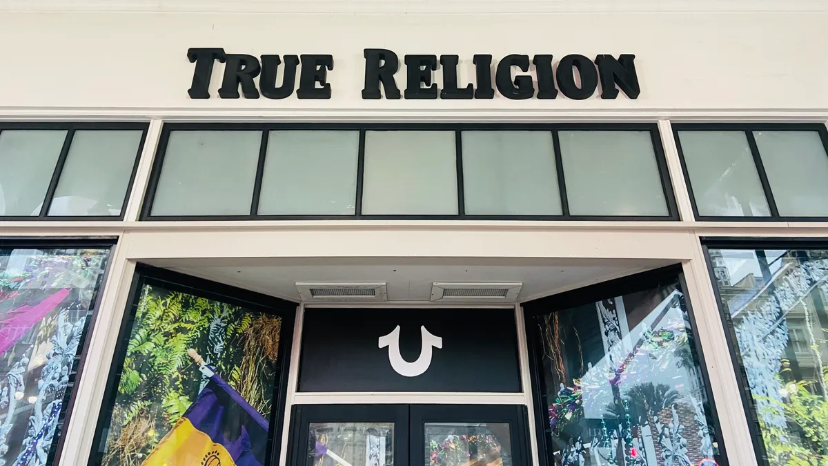 A storefront with colorful window decorations and a horseshoe emblem above the door, with the words "True Religion" in black, all-capital letters.