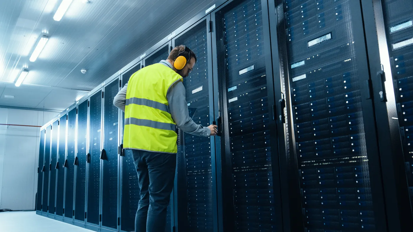 A data center technician with a high visibility vest opening the door to a server rack.