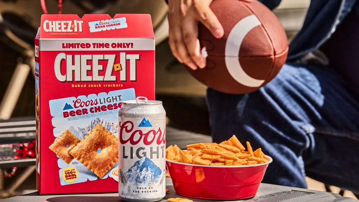 A box of Cheez-Its next to a Coors Light and a bowl, with a person holding a football.