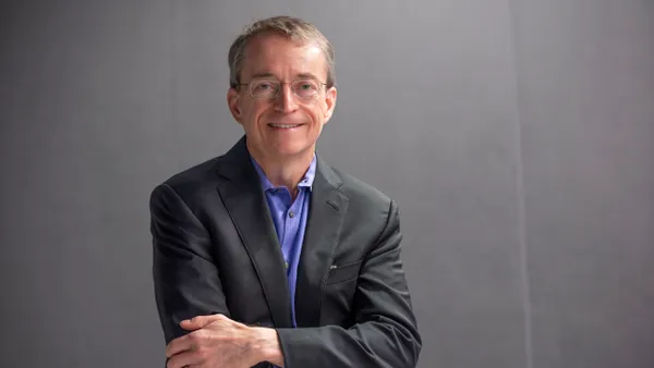 A headshot of a man in glasses, dark suit coat and blue shirt with a gray background.