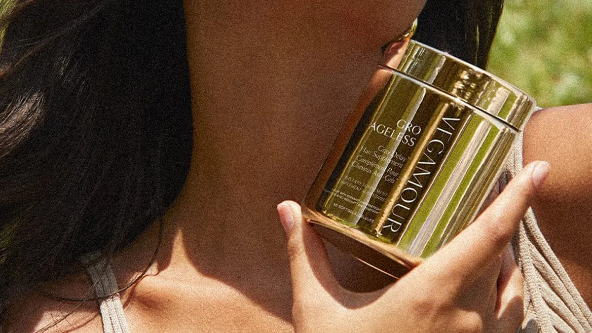 A brunette model holds a gold jar of Vegamour Gro product