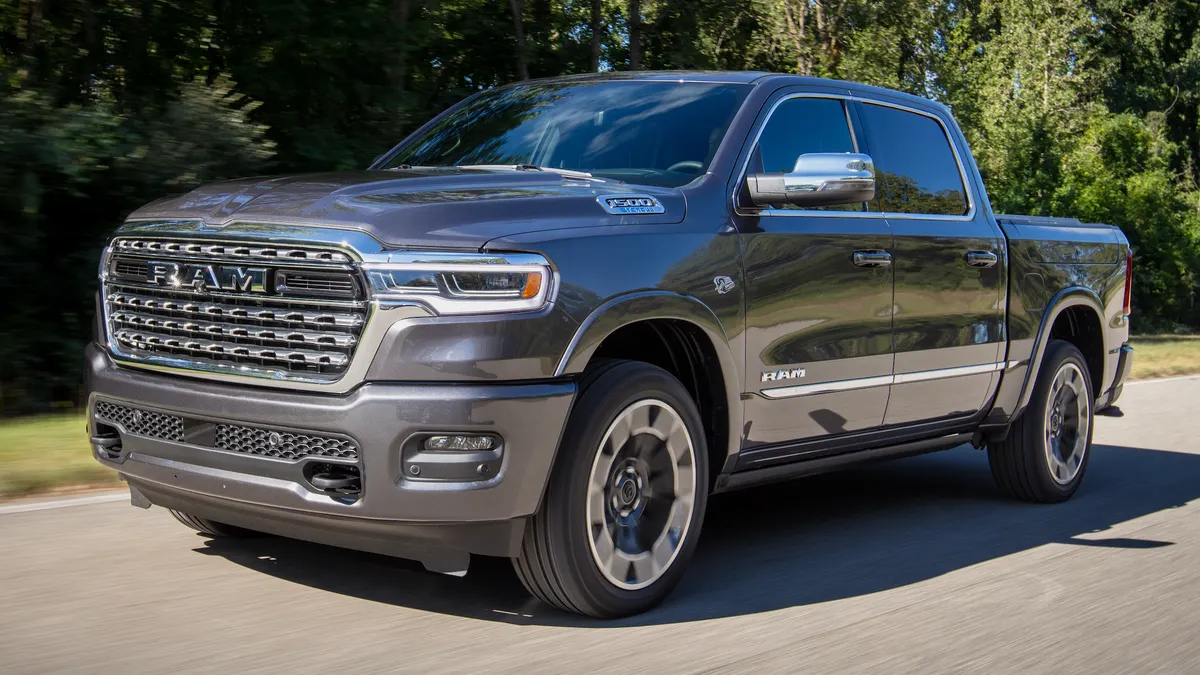 A 2026 Ram 1500 Limited pickup truck driving on a road with green trees in the background.