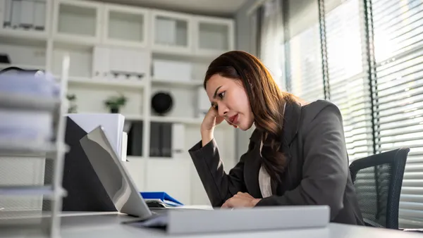 Attractive female employee sitting on desk table, feeling stressed and disappointed while work on laptop computer in corporate.