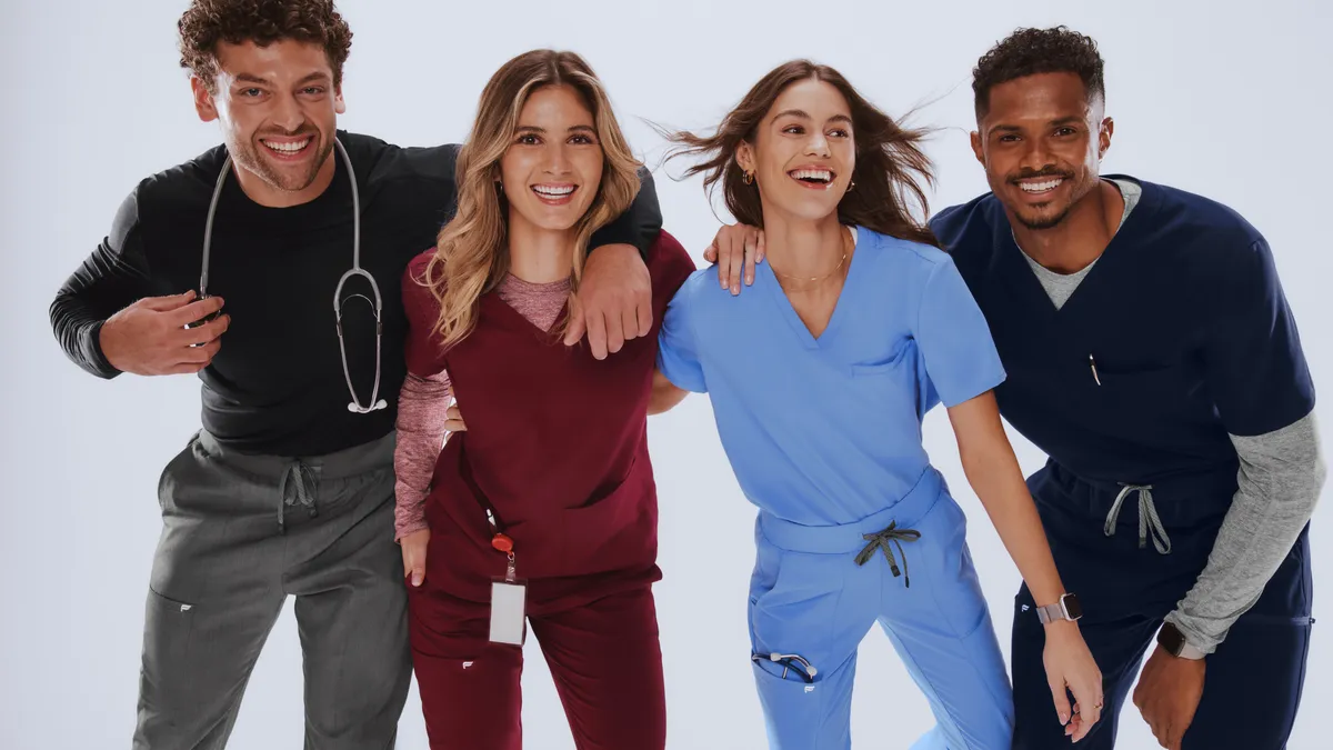 Four people smile at the camera wearing multi-colored medical scrubs