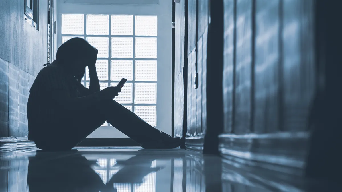 A photo of a person sitting on the floor of a hallway.