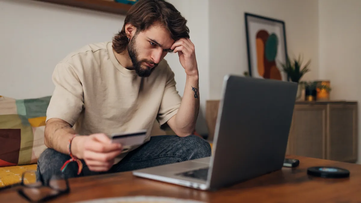 Worried man sitting on a couch looks at a laptop.