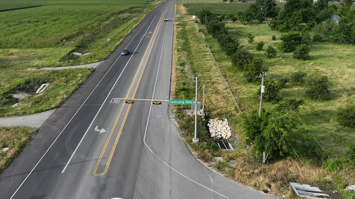 A road surrounded by greenlandscape, with a street light and green Samsung Hwy sign in the center.