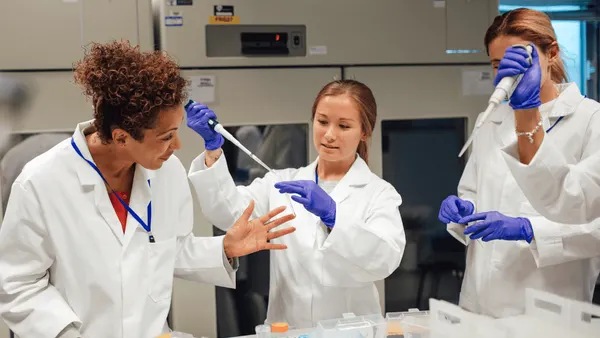 Three people in white coats working in a science lab
