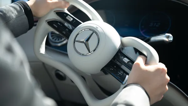 A driver's hands on the steering wheel of a Mercedes-Benz vehicle equipped with steer-by-wire technology.