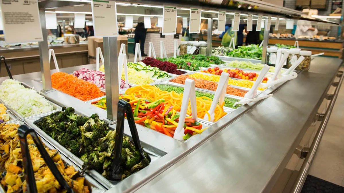 Whole Foods Market salad bar close-up with tongs sticking into the food