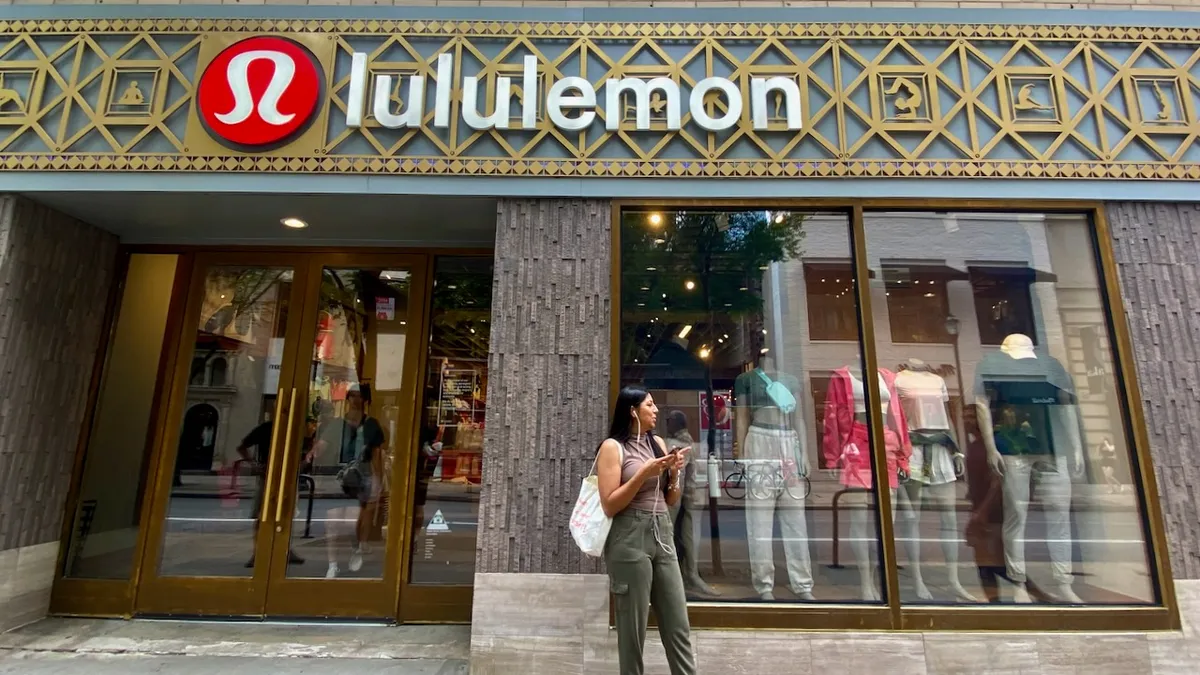 A person with white wired headphones and a white bag stands outside a clothing store.