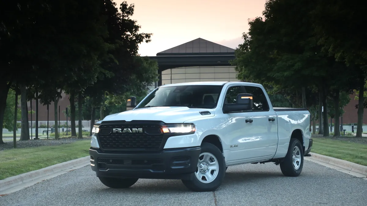 A white 2025 Ram 1500 Tradesman pickup parked outdoors with green trees in the background.