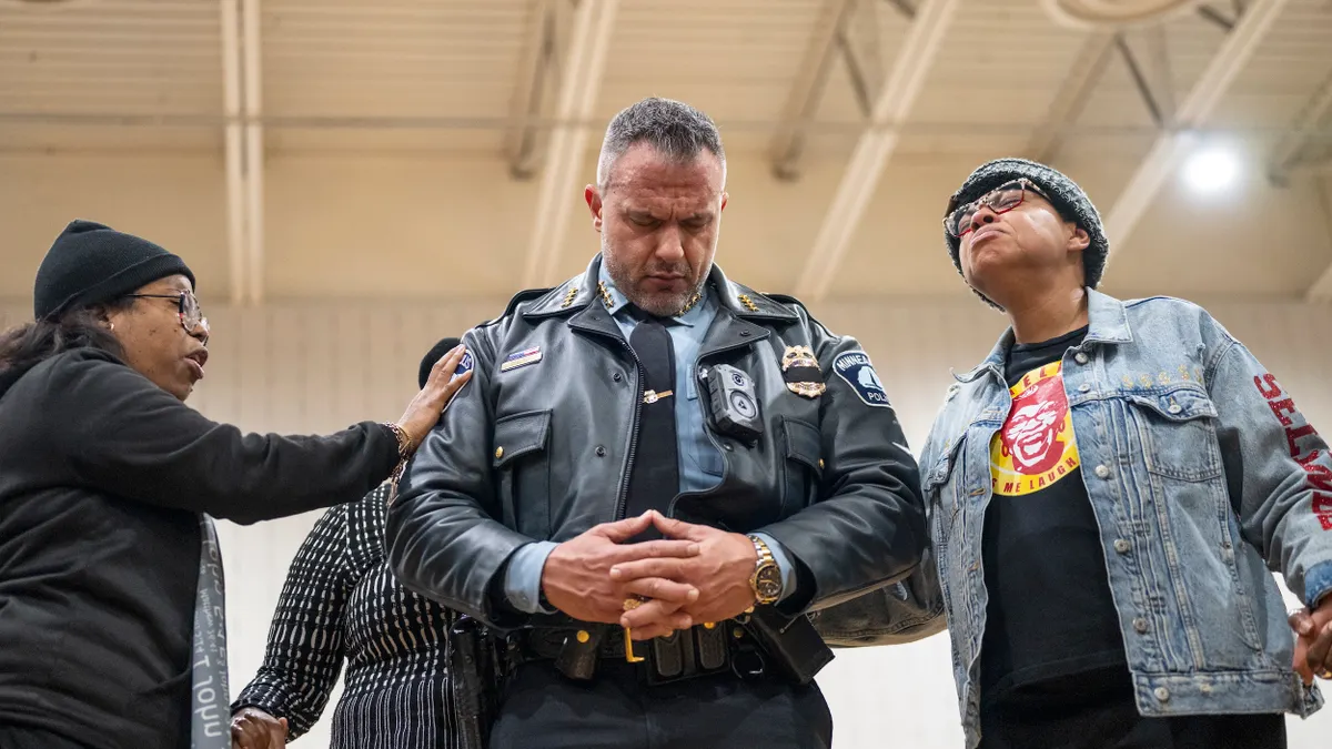 A person wearing a police uniform prays as two other people touch them.