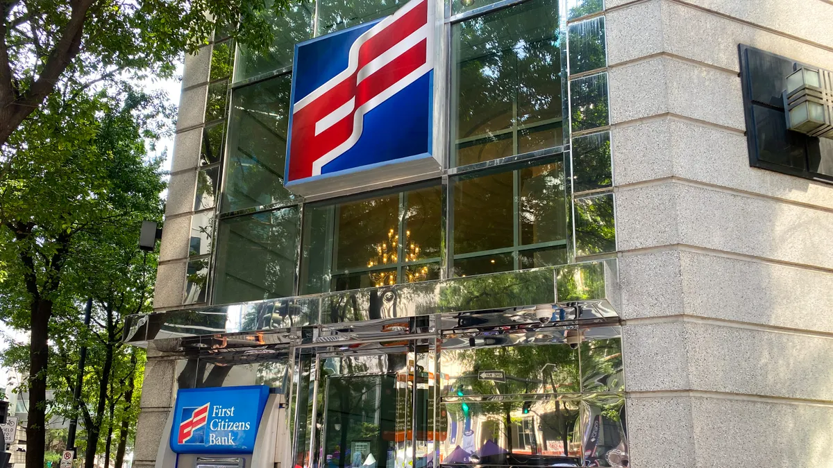 The "First Citizens" logo is shown above a doorway on a stone building with mirror panels. An ATM with the words "First Citizens Bank" sits next to the door.