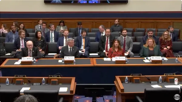 People seated at a long desk with others in four rows of seats behind them.