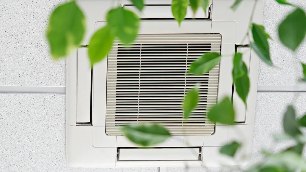 An air conditioning unit in a modern office, with a plant blurry in the foreground.