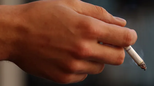 A photo of a hand holding a lit cigarette.