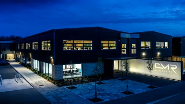 A nightime shot of the exterior of CMR Surgical's headquarters in Cambridge, U.K., with lights on in the windows of the two-story building.