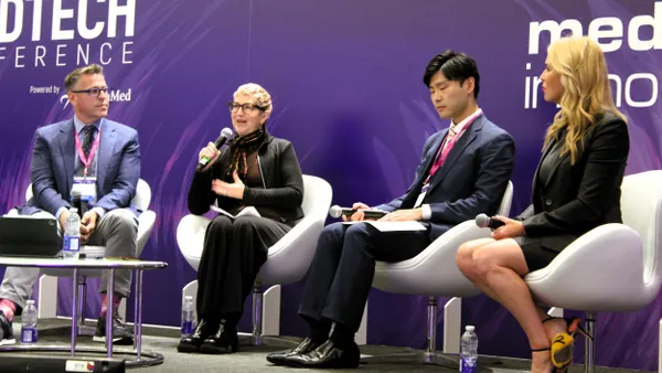 Four people sit side by side on a stage. The second person from the left holds a microphone and speaks.