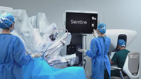 Three clinicians work with a robotic surgery system.