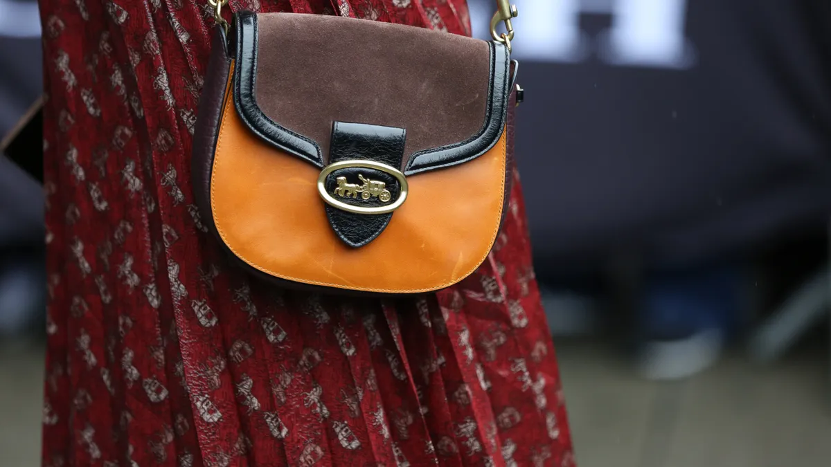 A person in a red floral skirt is holding aa orange, brown and black handbag with a Coach logo on it.