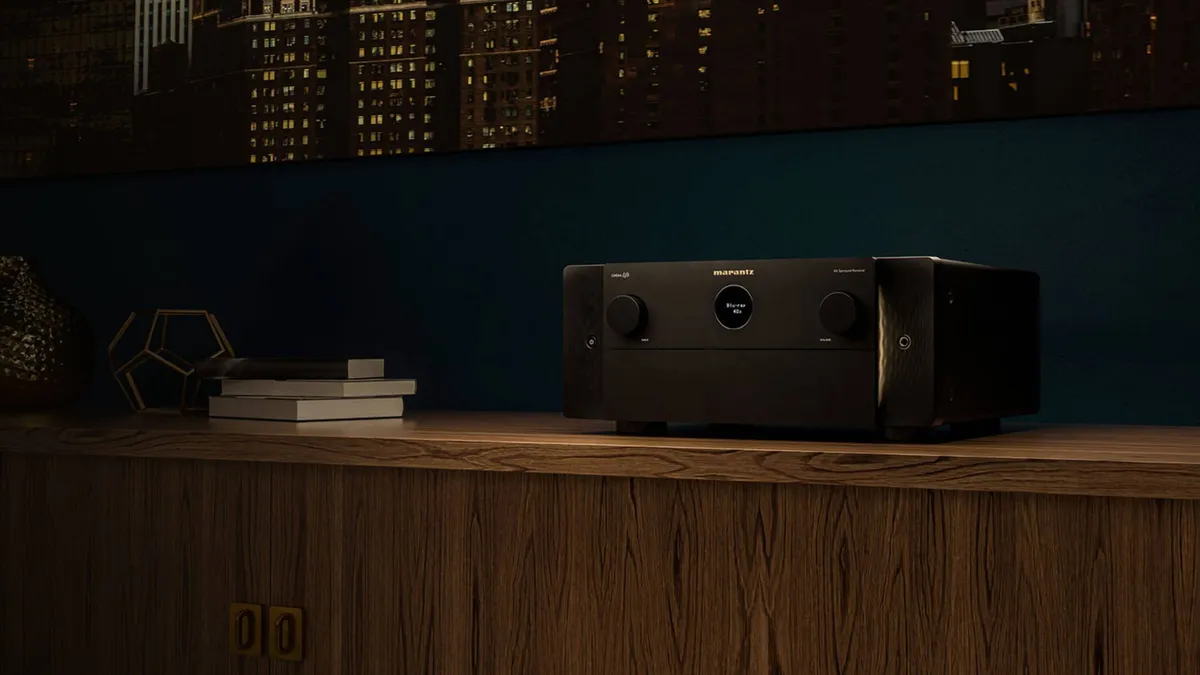 A Marantz home entertainment system is pictured on a wooden table top with a city skyline at nighttime visible in the background through a window.