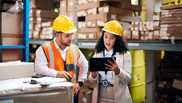 Two workers reviewing a tablet in a warehouse.