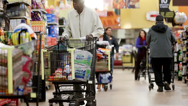 Seniors with shopping carts walk down a grocery aisle.