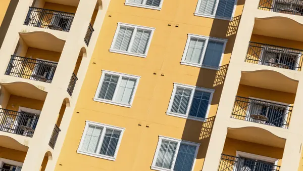 A close-up view of the exterior of a yellow apartment building with multiple floors, featuring a vertical row of windows surrounded by two rows of balconies.