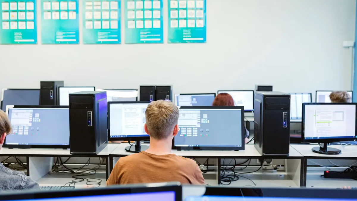 A row of students learning how to code while working at a classroom computer.