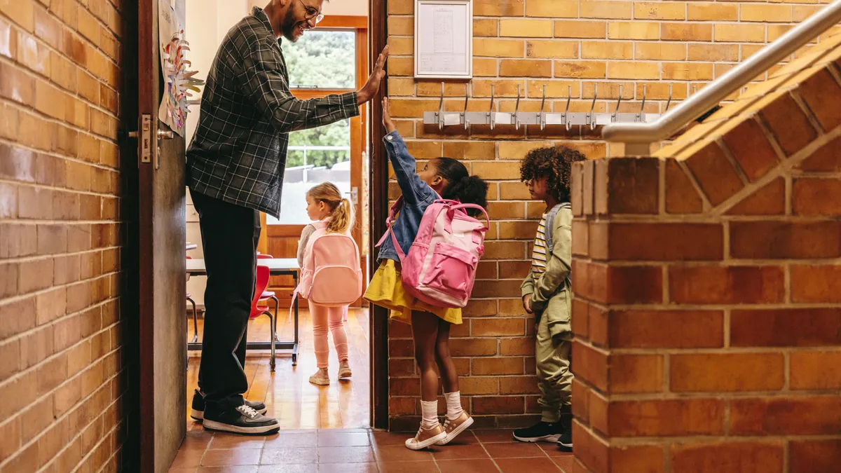 Elementary school teacher greeting his students at the door with a high five