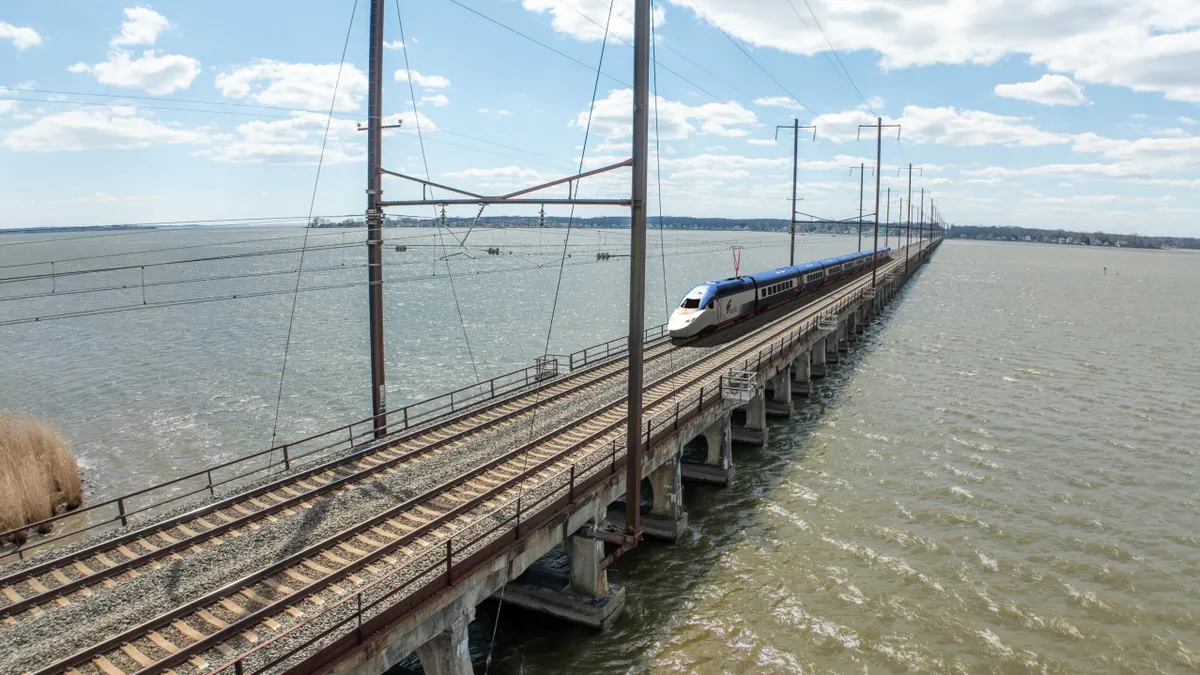 An elevated view shows a train crossing a bridge over a river.