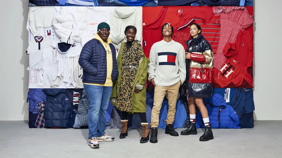 Four people wearing Tommy Hilfiger apparel stand smiling in front of a collection of clothes arranged by color to look like the brand's red, white and blue colorblock logo.