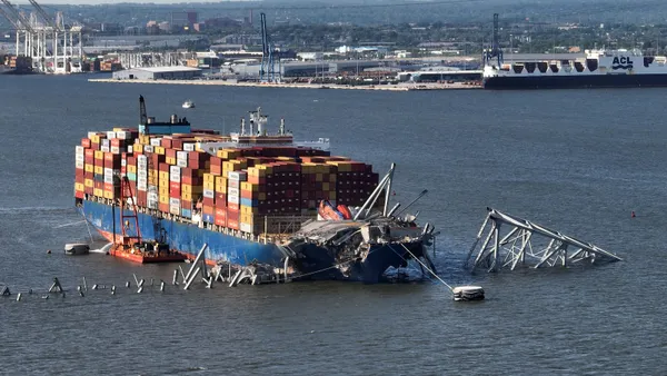 A massive cargo ship sits in the middle of a river surrounded by debris.