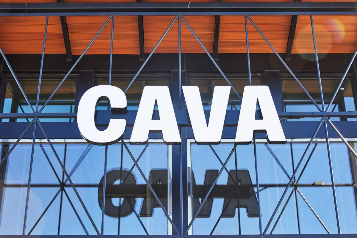 A white sign that says Cava in front of a glassed facade building.