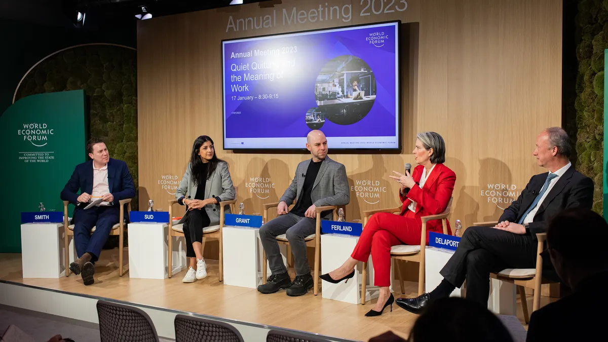 A group of people sit on a stage during a conference panel.