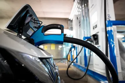 The front of a silver car is connected to an electric vehicle charger.