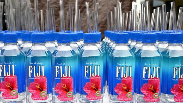 Bottles of Fiji Water branded waterbottles with straws coming out of the cap are placed in a line.