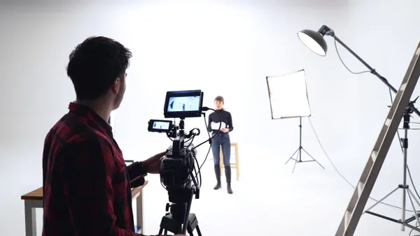 A cameraman films an actor reading from a script in a white studio space