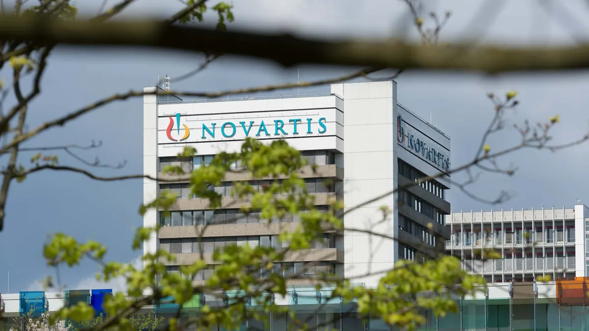 A sign reading Novartis is seen on the side of a building viewed through trees.