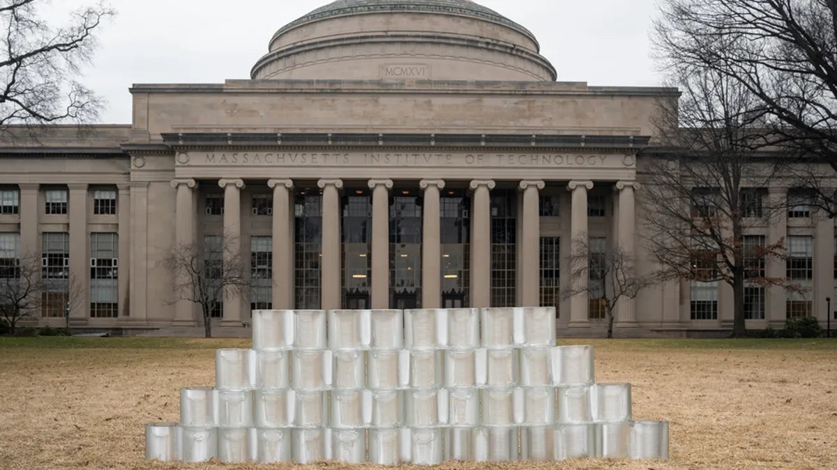 A wall of glass bricks sit on a lawn in front of an old building.