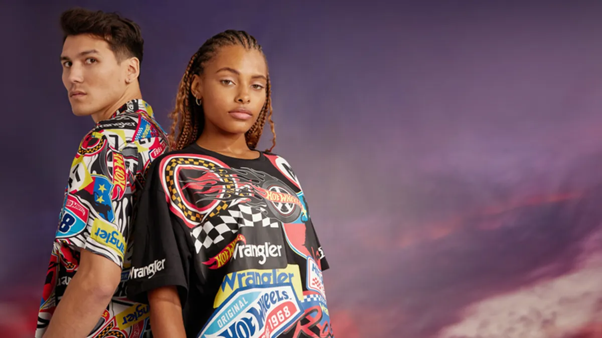 Two people stand back to back in front of a purple sky backdrop. They are wearing heavily logoed Hot Wheels and Wrangler shirts.