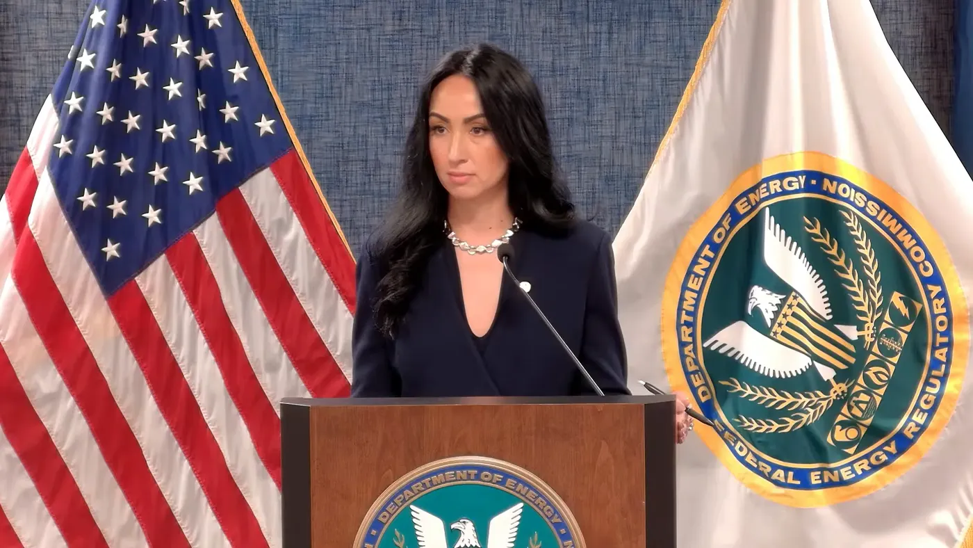 A woman stands at a podium if front of a US flag and a Federal Energy Regulatory Commission flag.
